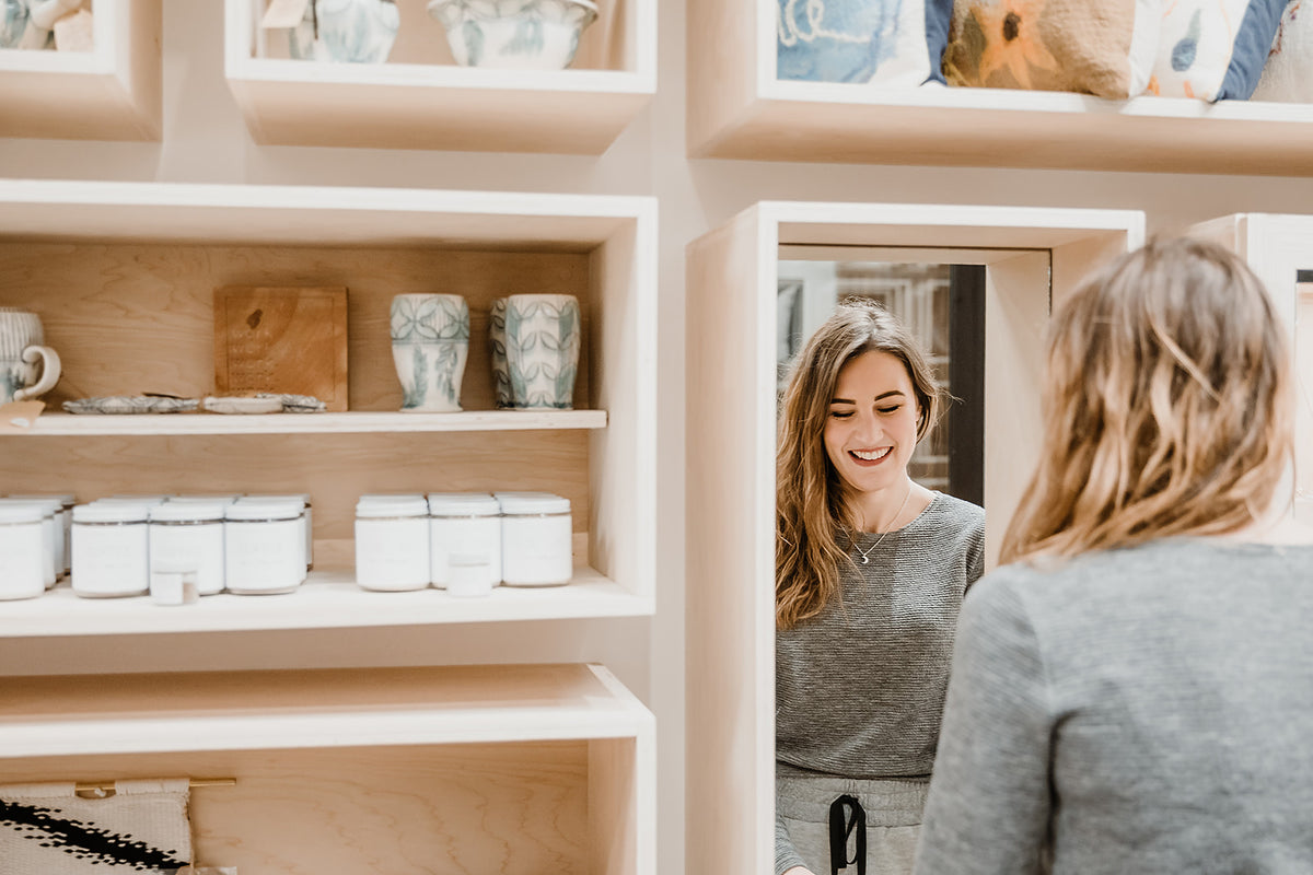 Beige wall with shelving full of store products and woman facing mirror